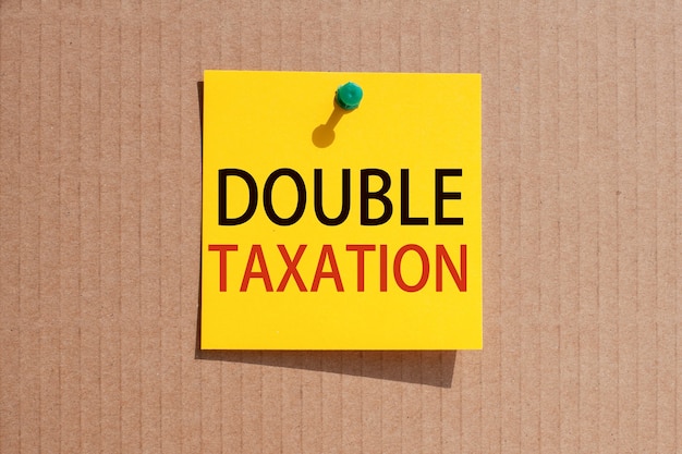 Fraza biznesowa - podwójne opodatkowanie - napisana na żółtym kwadratowym papierze i przypięta na tekturze