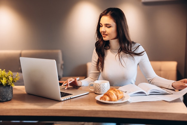 Freelance Student Kobieta Za Pomocą Laptopa Siedząc W Domu. Młoda Kobieta Siedzi W Kuchni I Pracuje Online Na Laptopie. ładna Kobieta Pije Herbatę Podczas Pracy.