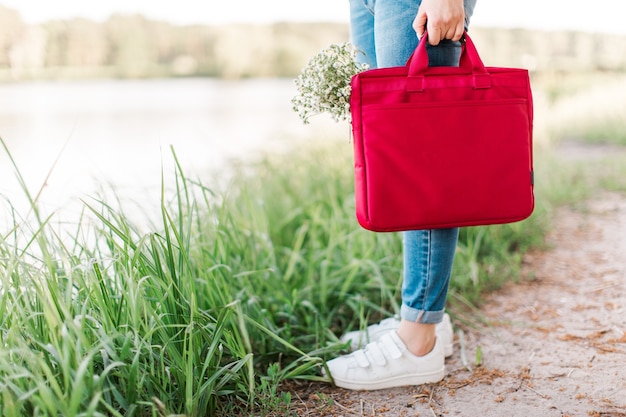 Zdjęcie freelancer dziewczyna pracuje z laptopem na zewnątrz w pobliżu wody. dziewczyna trzyma czerwoną torbę biznesową