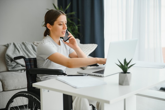 Freelancer na wózku inwalidzkim, korzystający z laptopa w pobliżu notebooka i dokumentów na stole