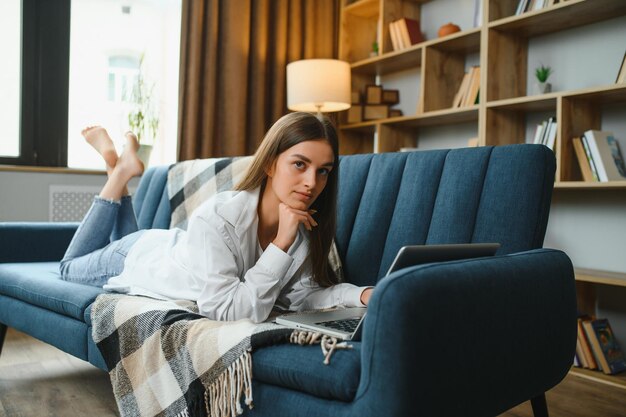 Freelancer pracujący na laptopie w domu leżący na wygodnej beżowej sofie