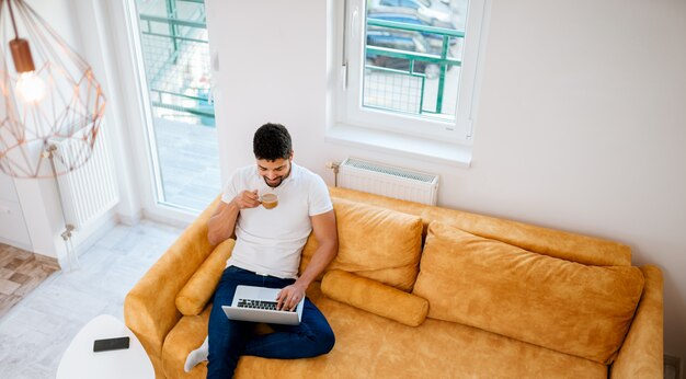 Freelancer pracuje na laptopie siedząc na kanapie, widok z góry.