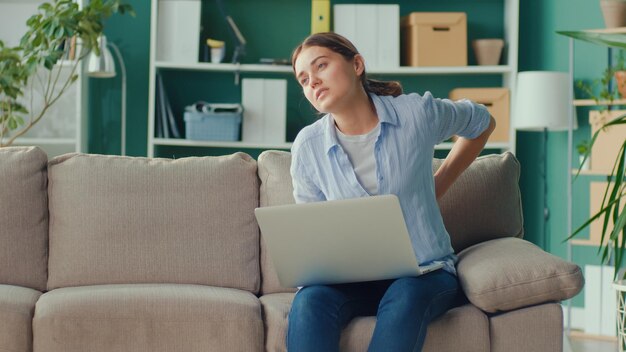 Freelancer Siedzący Na Kanapie, Pracujący Zdalnie Z Domu, Nagle Odczuwa Ból