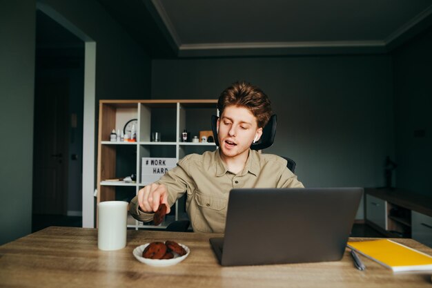 Freelancer siedzi w domu w pracy z laptopem i zajada ciasteczka z herbatą Praca zdalna w domu