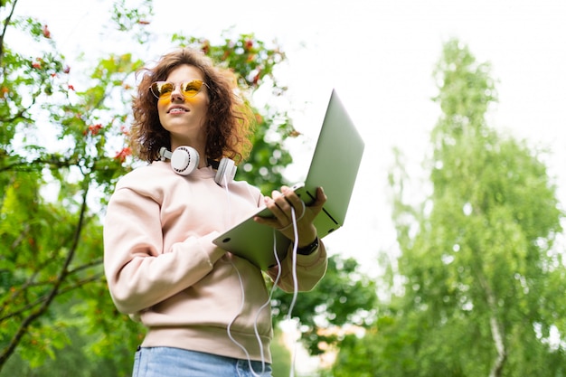 Freelancer Stoi W Parku Z Laptopem I Słuchawkami W Centrum Parku Wśród Drzew