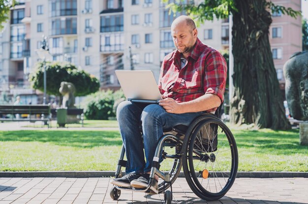 Freelancer z niepełnosprawnością ruchową na wózku inwalidzkim pracujący w parku