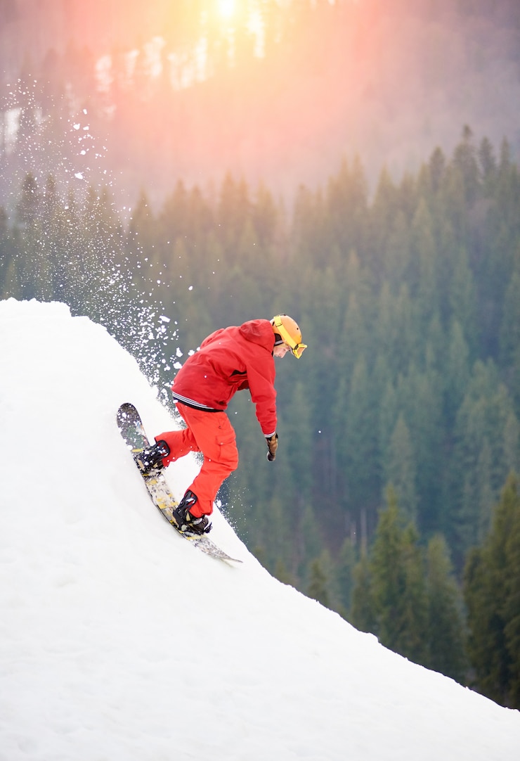 Zdjęcie freerider w snowboardzie w czerwonym kolorze, jadący ze szczytu ośnieżonego wzgórza z deską snowboardową