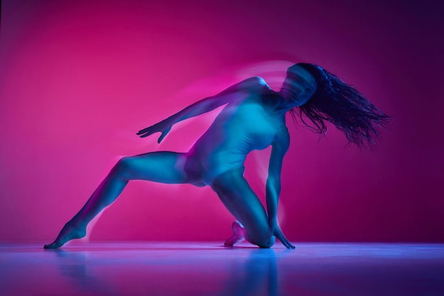 Freestyle zmysłowość młoda kobieta tańcząca w garniturze nad gradientem różowym tłem studyjnym w neonie
