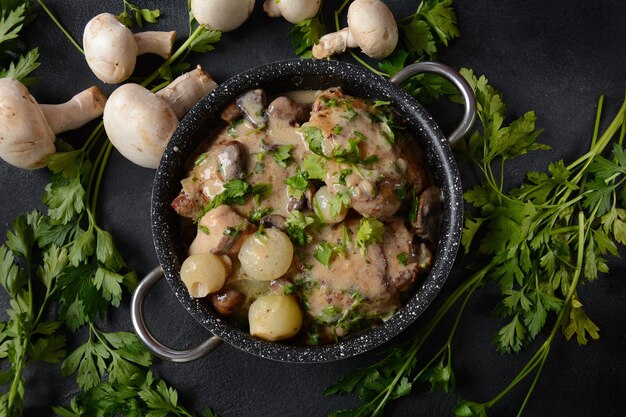 Zdjęcie fricassee - kuchnia francuska. kurczak duszony w kremowym sosie z pieczarkami na patelni żaroodpornej na czarnym stole