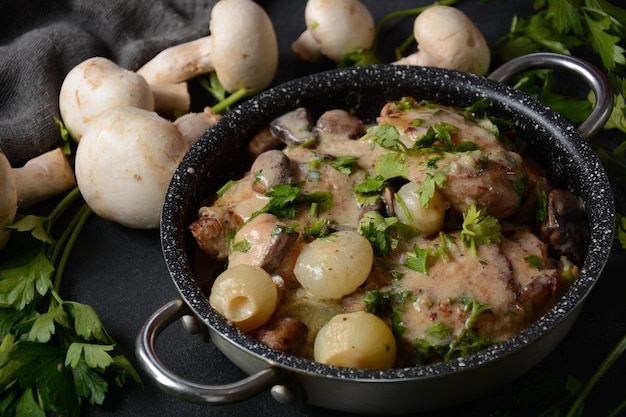 Fricassee - kuchnia francuska. Kurczak duszony w kremowym sosie z pieczarkami na patelni żaroodpornej na czarnym stole