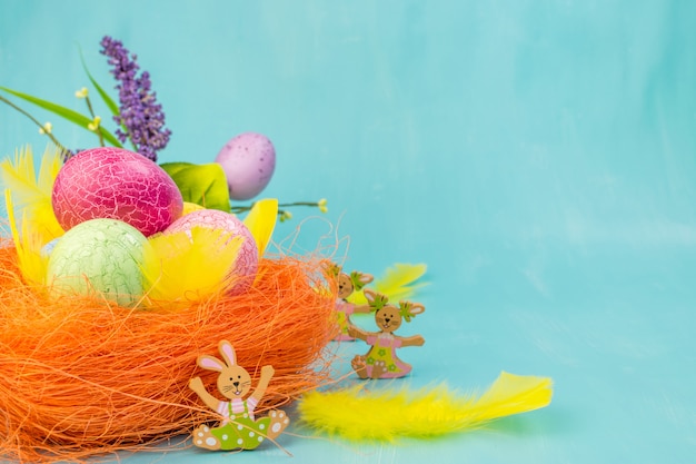 Zdjęcie frontowy widok kolorowi easter jajka w pomarańcze gniazduje z wiosna kwiatami i żółtymi piórkami na turkusowym tle z wiadomości przestrzenią