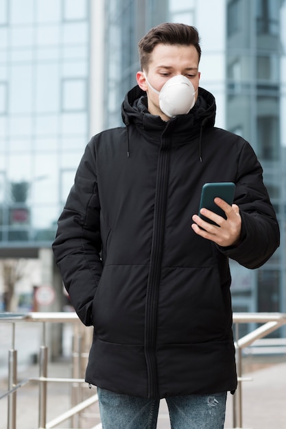 Zdjęcie frontowy widok mężczyzna patrzeje jego telefon w mieście z medyczną maską