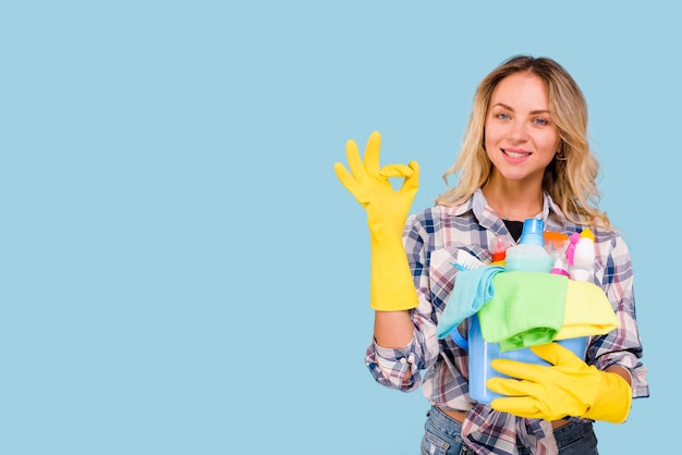 Frontowy Widok Pokazuje Ok Znaka Piękna Kobieta Podczas Gdy Trzymający Cleaning Produkty W Wiadrze Przeciw Błękitnemu Tłu