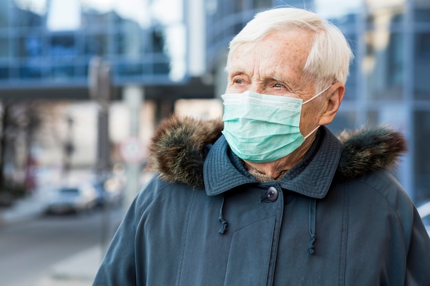 Zdjęcie frontowy widok starsza kobieta jest ubranym medyczną maskę w mieście