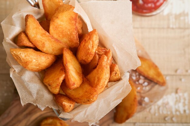 Frytki w metalowym drucianym koszu z solą i keczupem na starym drewnianym jasnym tle clous up Smażone ziemniaki Koncepcja fast food i niezdrowej żywności