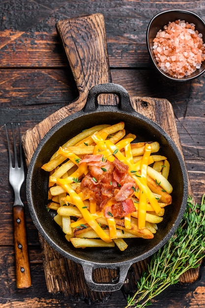 Frytki Z Roztopioną Mieszanką Sera Cheddar I Boczku Podane Na Patelni. Ciemny Drewniany Stół. Widok Z Góry.