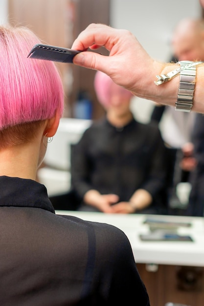 Fryzjer czesze farbowane na różowo krótkie włosy klientki w widoku z tyłu salonu fryzjerskiego