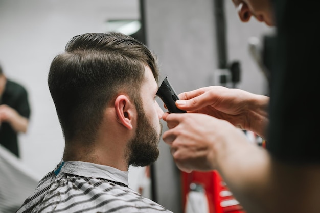 Fryzjer do zdjęć z bliska tworzy stylową fryzurę dla brodatego mężczyzny używa trymera