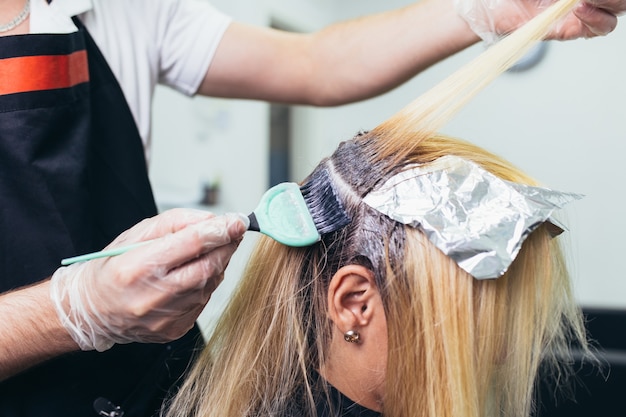 Zdjęcie fryzjer farbuje kobiece włosy, robiąc pasemka swojemu klientowi folią