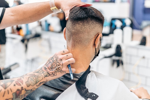 Fryzjer golący włosy na karku dorosłego mężczyzny rasy kaukaskiej siedzi na krześle w zakładzie fryzjerskim