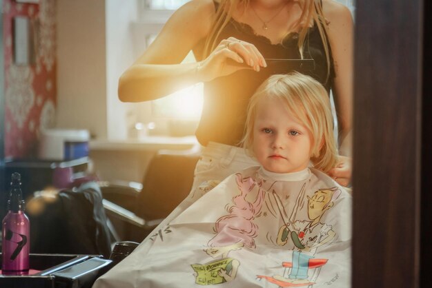 Zdjęcie fryzjer kobieta robi modną ładną fryzurę dla ślicznej małej blond dziewczynki
