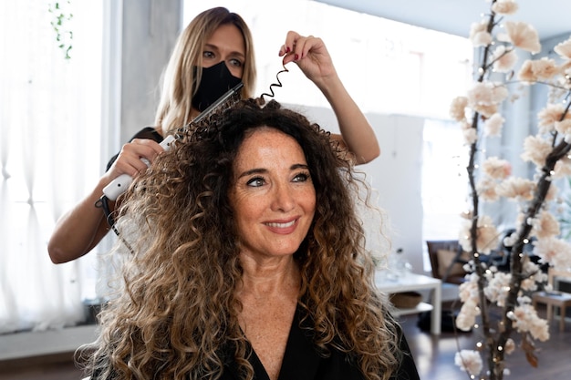 Fryzjer kręcący włosy dojrzałej kobiety za pomocą lokówki elektrycznej