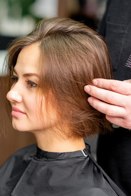 Fryzjer męski pracuje nad fryzurą młodej brunetki kaukaskiej kobiety w salonie fryzjerskim.