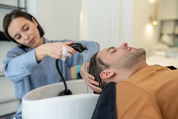 Fryzjer myjący włosy klientowi męskiemu w salonie kosmetycznym