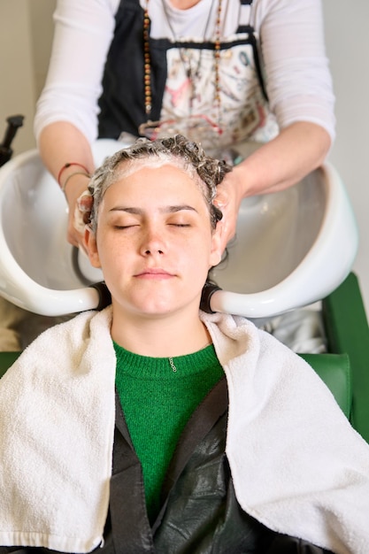 Zdjęcie fryzjer myje głowę brunetki szamponem w salonie kosmetycznym