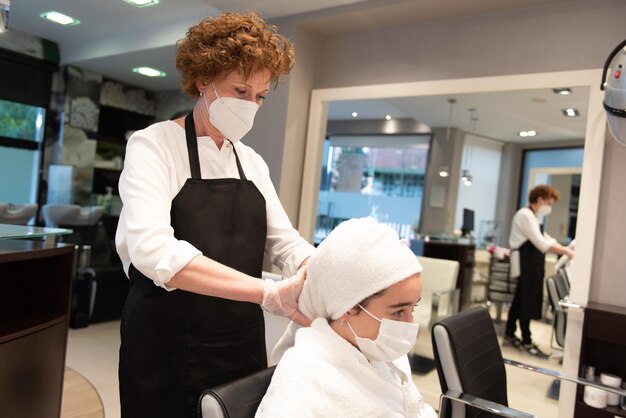 Fryzjer nakłada ręcznik na włosy nastolatki noszącej maskę