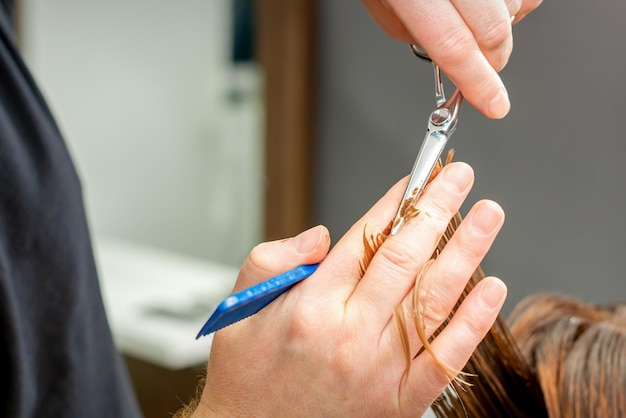 Fryzjer obcina włosy brunetce. Fryzjer jest strzyżenie włosów klientki w profesjonalnym salonie fryzjerskim, z bliska.