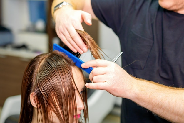 Fryzjer obcina włosy brunetce. Fryzjer jest strzyżenie włosów klientki w profesjonalnym salonie fryzjerskim, z bliska.