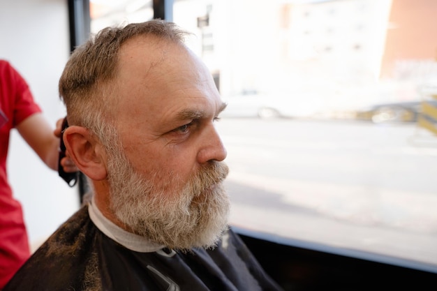 Fryzjer przycinanie i cięcie brodaty mężczyzna z maszyną do golenia w procesie fryzjerskim Fryzura