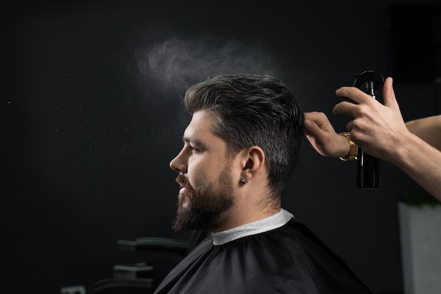 Fryzjer robi fryzurę dla pewnej siebie brodatej hipsterki. Reklama dla fryzjera i salonu kosmetycznego dla mężczyzn.