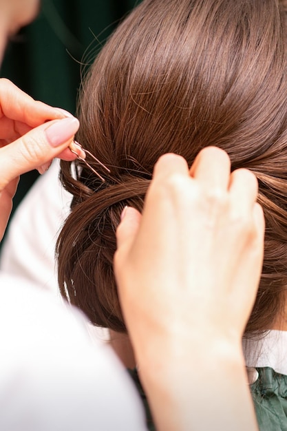 Fryzjer robi fryzurę młodej brunetki w salonie fryzjerskim, z bliska.