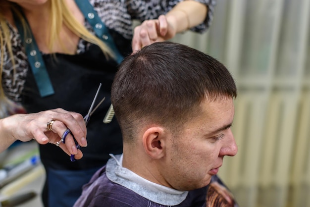 Fryzjer robi fryzurę młodemu mężczyźnie w salonie kosmetycznym