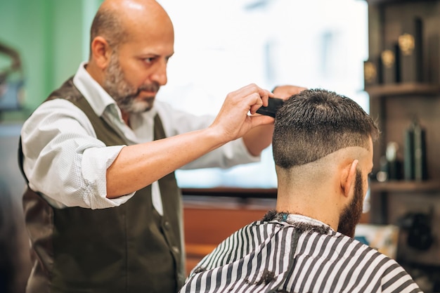Fryzjer strzyżący włosy klienta w salonie fryzjerskim