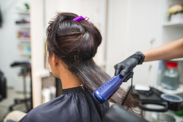 Fryzjer używający prostowanych włosów do prostowania włosów Stylistka włosów pracująca nad kobiecą fryzurą w saloniePielęgnacja włosów Piękna atrakcyjna kobieta w salonie kosmetycznym