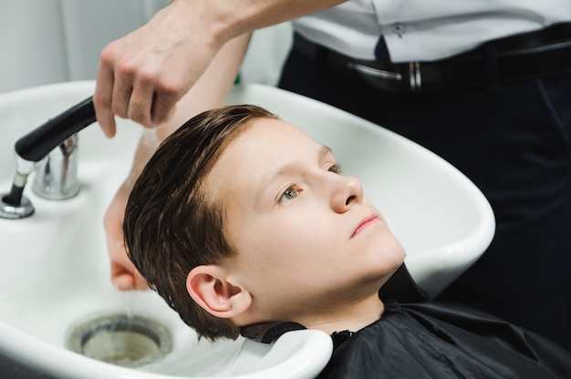 Fryzjer w zakładzie fryzjerskim myje chłopca