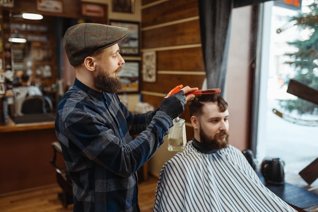 Fryzjer z grzebieniem i maszynką elektryczną robi fryzurę klientce. Profesjonalny fryzjer to modne zajęcie. Fryzjer męski i klient w salonie fryzjerskim w stylu retro