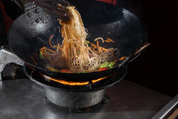 Zdjęcie funchoza flambe makaron ryżowy z warzywami gotowanie na ogniu na patelni wok. uliczne jedzenie.