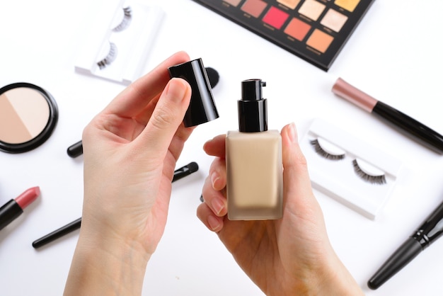 Fundacja w rękach kobiety. Profesjonalne produkty do makijażu zawierające kosmetyki kosmetyczne, podkład, szminkę, cienie do powiek, rzęsy, pędzle i narzędzia.