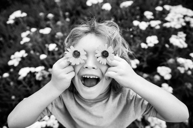 Funny Boy Kid and Daisies Szczęśliwe małe dziecko o blond włosach z kwiatami i oczami na trawie ze stokrotkami