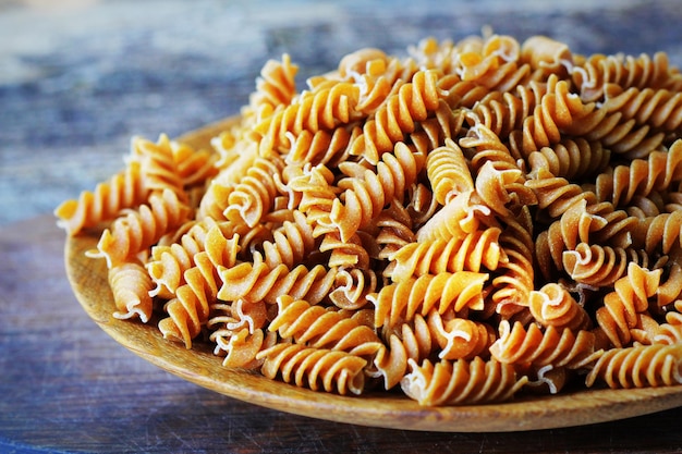 Fusilli pełnoziarniste na talerzu, makaron na drewnianym stole.