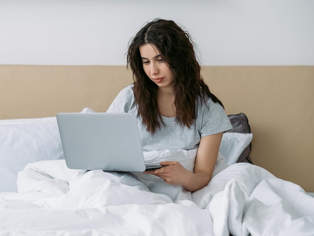 Gadżetowy poranek Praca zdalna Praca online Freelancer Styl życia Zrelaksowana pewna siebie kobieta korzystająca z laptopa w białym łóżku w jasnej sypialni w domowym biurze