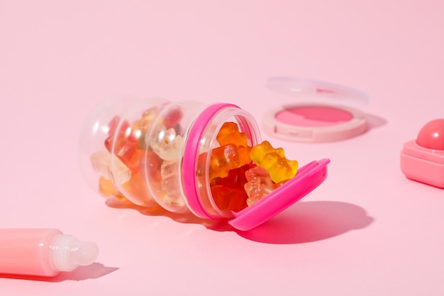 Galaretowe cukierki w słoiku i kosmetyki dekoracyjne na różowym tle z bliska