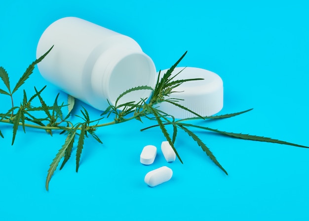 Zdjęcie gałąź marihuany z zielonymi liśćmi i białym plastikowym słoikiem z owalnymi tabletkami