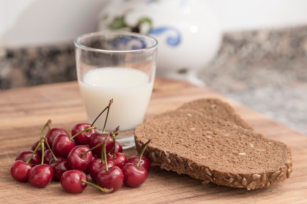 Garść wiśni szklanka mleka i kromki chleba żytniego z pestkami na śniadanie