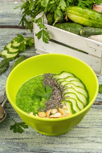 Gazpacho ogórkowe. Zielona świeża zimna letnia zupa. Świeże warzywa, warzywa, przyprawy i sztućce. Stare drewniane deski tło, z bliska