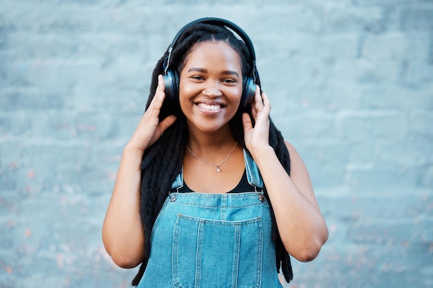 Gen z czarna kobieta słuchawki muzyczne i portret na tle ściany w mieście Nigerii słuchanie radia audio i dźwięk Szczęśliwa młoda afrykańska studentka wolność i streaming miejskiego podcastu na świeżym powietrzu